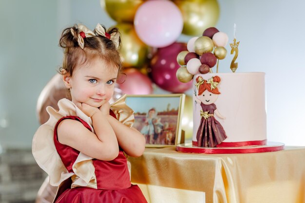 Portrait d'un bébé mignon de deux ans avec les mains sous le menton souriant et célébrant son anniversaire. Belle séance photo d'anniversaire de petite fille