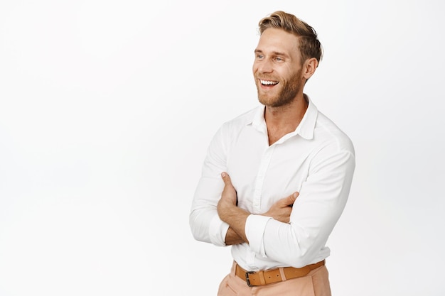 Portrait de bel homme adulte blond mec fort en chemise blanche bras croisés sur la poitrine en riant et en souriant tout en regardant de côté fond blanc