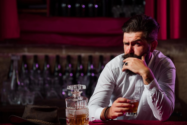 Portrait d'un bel homme d'affaires barbu en costume élégant buvant un whisky