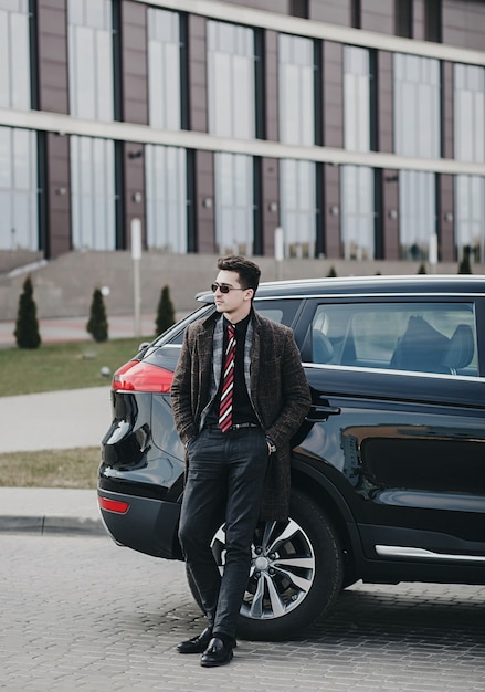 Portrait d'un bel homme d'affaires debout près de la voiture à l'extérieur près d'un bâtiment moderne