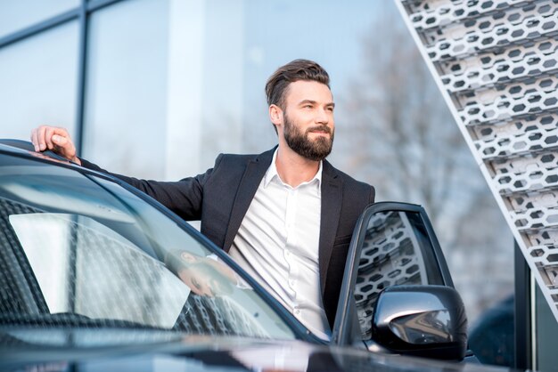 Portrait d'un bel homme d'affaires debout près de la voiture à l'extérieur près de la façade du bâtiment moderne