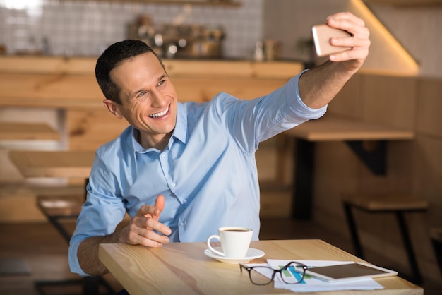 Portrait d'un bel homme d'affaires heureux prenant un selfie avec un smartphone au café