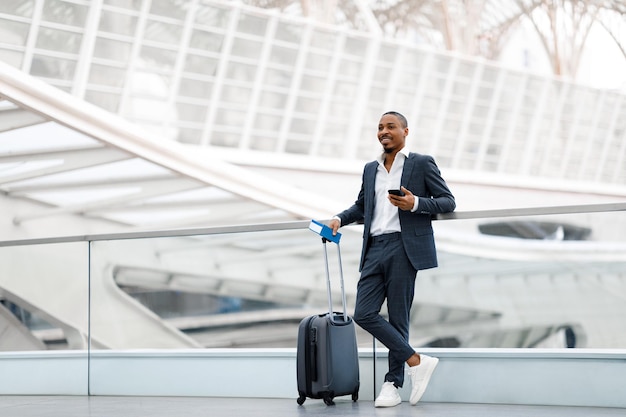 Portrait d'un bel homme d'affaires noir debout avec une valise au terminal de l'aéroport