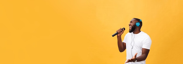 Portrait d'un bel homme africain chic positif joyeux tenant un microphone et ayant des écouteurs sur
