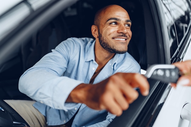 Photo portrait d'un bel homme afro-américain heureux assis dans sa voiture nouvellement achetée close up