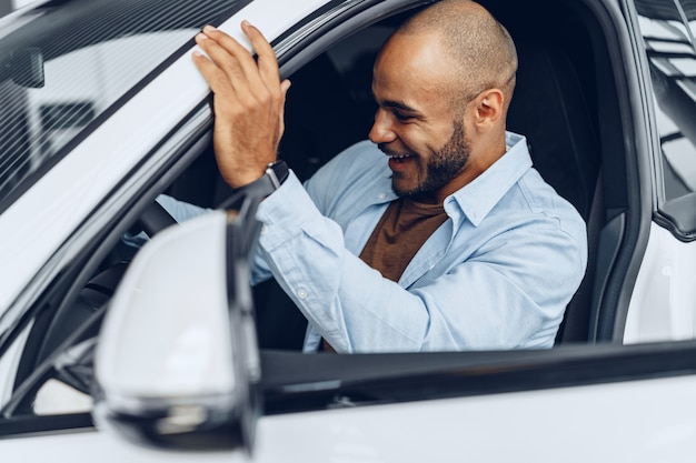 Portrait d'un bel homme afro-américain heureux assis dans sa voiture nouvellement achetée close up