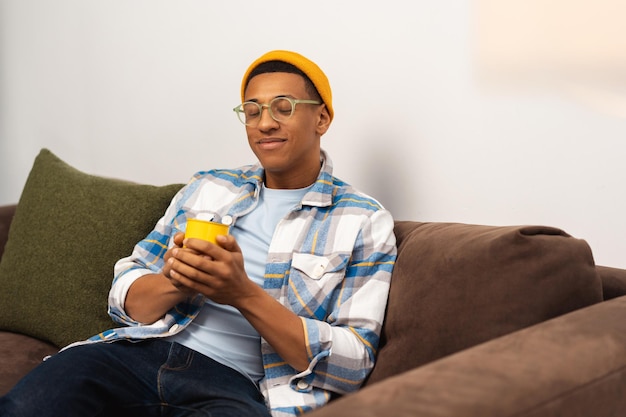 Portrait d'un bel homme afro-américain souriant portant un chapeau jaune élégant tenant une tasse de café