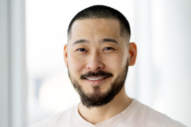 Portrait d'un bel homme asiatique souriant avec une barbe élégante et une coiffure regardant la caméra