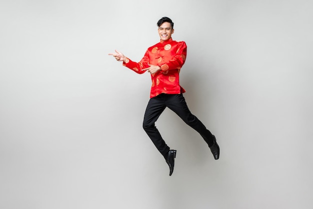 Portrait d'un bel homme asiatique souriant en tenue traditionnelle chinoise souriant et pointant les mains vers un espace vide de côté dans un fond de studio isolé gris clair