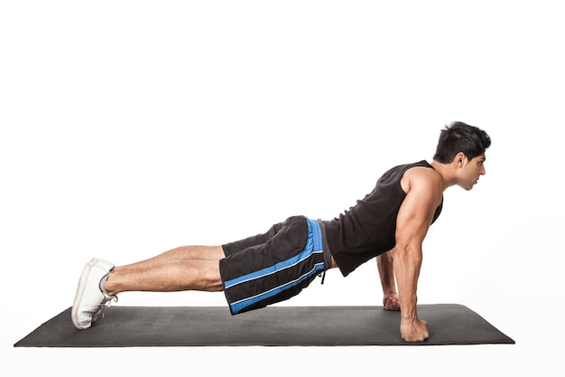 Portrait d'un bel homme athlétique fort debout en position de planche travaillant sur un tapis de fitness faisant de l'exercice Phalakasana sur les bras droits Prise de vue en studio intérieur isolé sur fond blanc