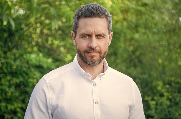 Portrait d'un bel homme au visage non rasé en chemise blanche à fond naturel