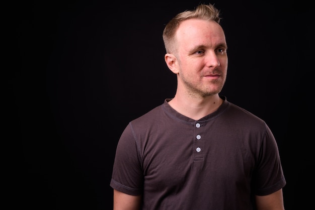 Portrait de bel homme aux cheveux blonds contre le mur noir