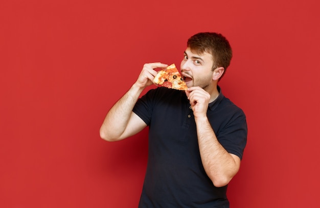 Portrait de bel homme avec barbe se dresse avec un morceau de pizza dans ses mains