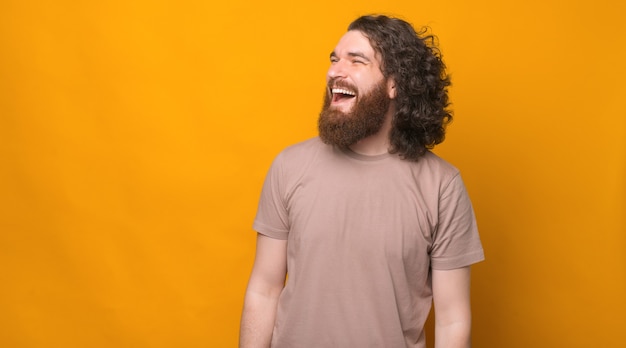 Portrait de bel homme barbu aux longs cheveux bouclés riant sur jaune