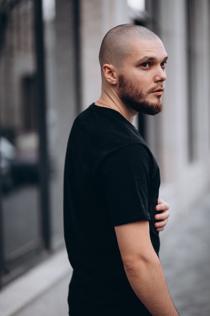 Portrait d'un bel homme barbu chauve dans un t-shirt noir dans la rue, qui regarde ailleurs