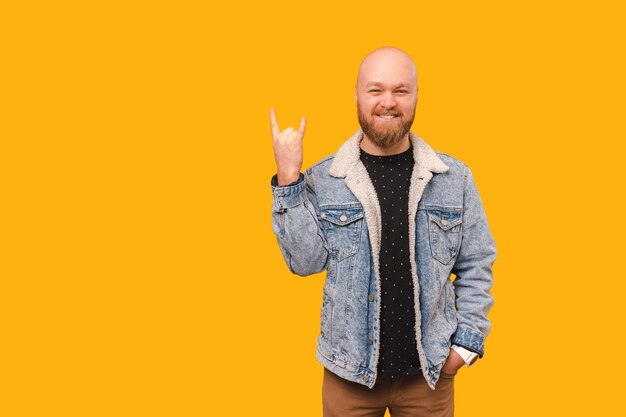 Portrait d'un bel homme barbu chauve montrant un geste rock dans un studio