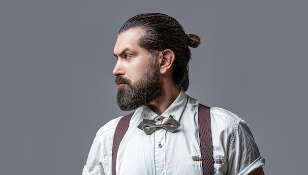 Portrait d'un bel homme barbu en chemise blanche et bretelles noeud papillon Homme en chemise corrigeant sa cravate colorée