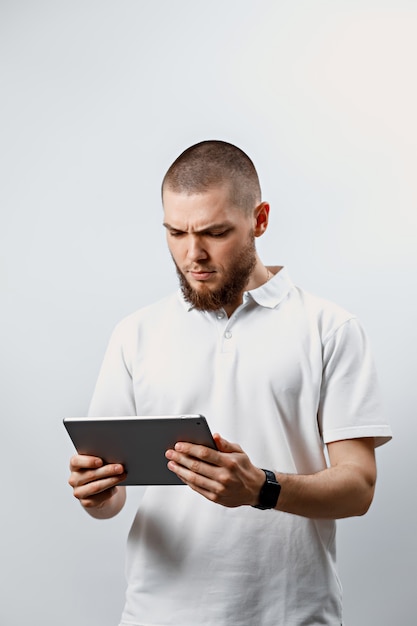 Portrait d'un bel homme barbu dans un t-shirt blanc en regardant une tablette