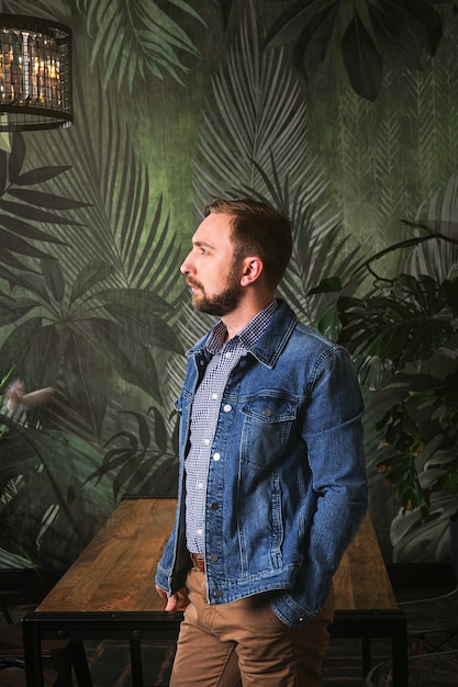 Portrait de bel homme barbu dans des vêtements décontractés élégants denim jacketstanding dans un appartement moderne