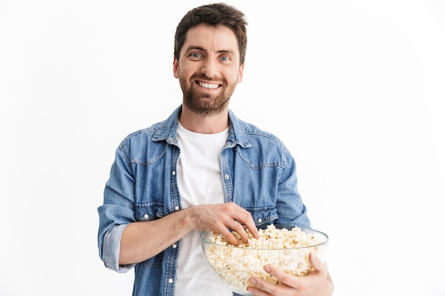 Portrait d'un bel homme barbu excité portant des vêtements décontractés, isolé, regardant un film, mangeant du pop-corn