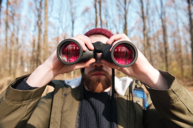 Portrait d'un bel homme barbu portant un chapeau regardant une vitre de champ dans la forêt.