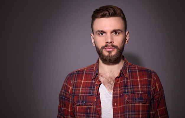 Portrait d'un bel homme barbu souriant dans une chemise à carreaux rouge sur fond gris