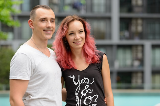 Portrait de bel homme et belle femme aux cheveux roses en couple ensemble dans la zone de la piscine à l'extérieur