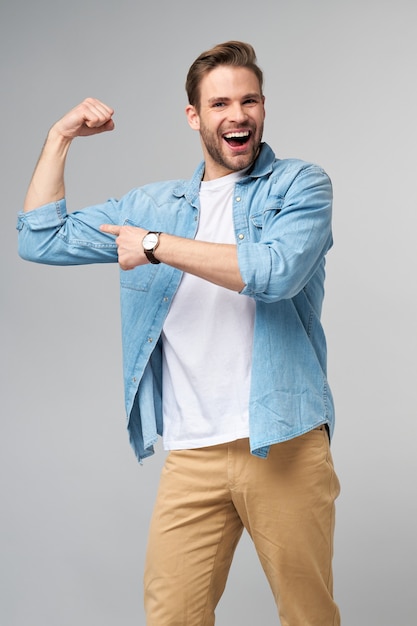 Portrait d'un bel homme en chemise de jeans montrant son biceps avec bras plié