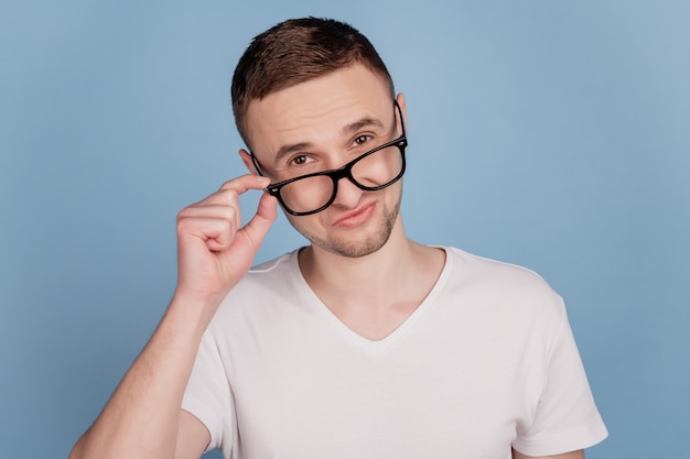 Portrait d'un bel homme confiant et intelligent touchant ses lunettes isolées sur fond de couleur bleu