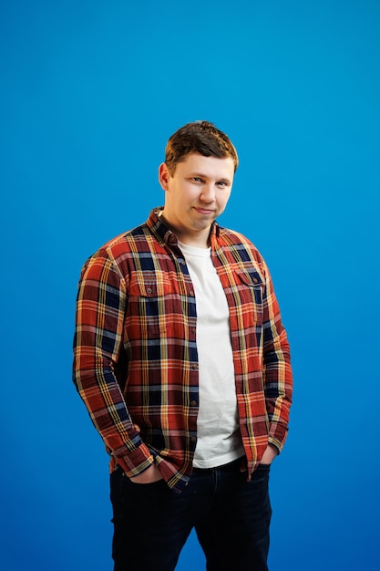 Portrait d'un bel homme européen en chemise regardant la caméra debout sur fond de studio bleu