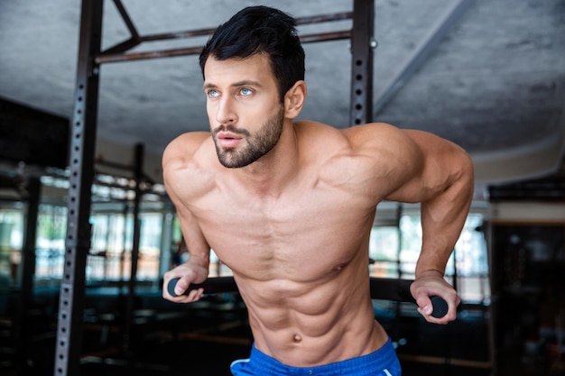 Portrait d'un bel homme faisant de l'exercice sur des barres parallèles dans une salle de fitness