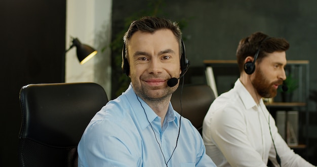 Photo portrait de bel homme heureux en casque travaillant à l'ordinateur dans le centre d'appels. les opérateurs masculins collègues de soutien au bureau.