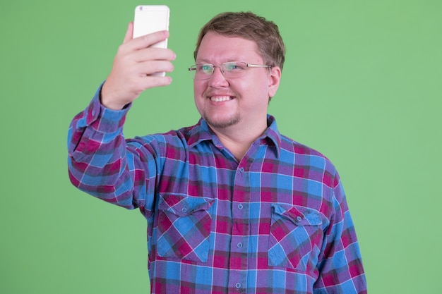 Portrait de bel homme hipster barbu en surpoids avec des lunettes contre clé chroma ou mur vert