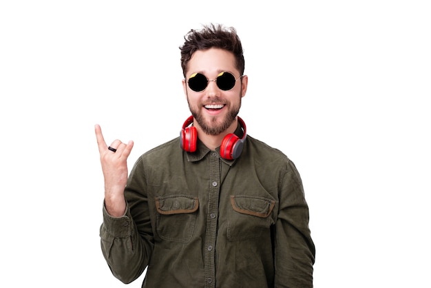 Portrait d'un bel homme avec des lunettes de soleil et des écouteurs, faisant un geste rock sur fond blanc