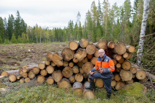 Portrait de bel homme mature tenant le téléphone et la hache du bois coupé à l'extérieur de la forêt