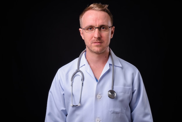 Portrait de bel homme médecin aux cheveux blonds contre le mur noir