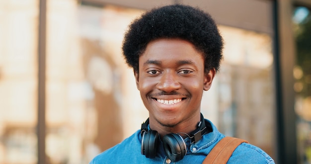 Portrait d'un bel homme multiracial afro-américain montrant un sourire charmant et des dents saines tout en marchant avec son smartphone dans la rue. Concept de personnes et de gadgets