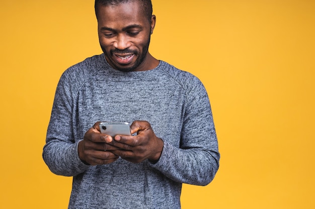 Portrait d'un bel homme noir afro-américain joyeux et joyeux, portant un envoi décontracté et recevant des messages isolés sur fond jaune. Utilisation du téléphone.