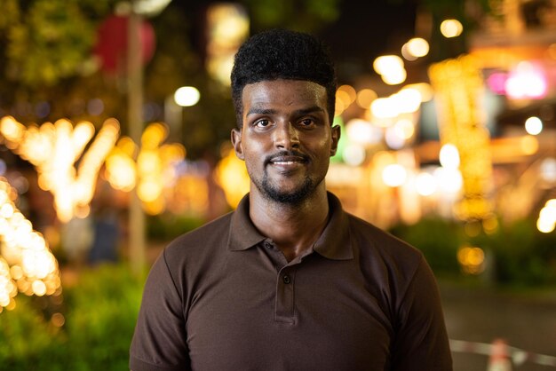 Portrait d'un bel homme noir en ville la nuit en souriant