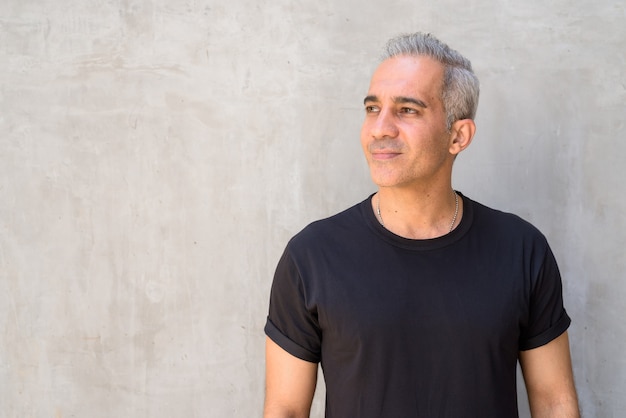 Portrait de bel homme persan aux cheveux gris contre le mur de béton à l'extérieur