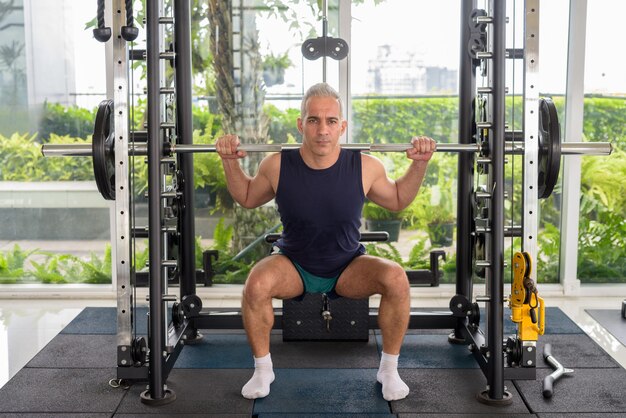 Portrait d'un bel homme persan mature aux cheveux gris faisant de l'exercice dans la salle de sport