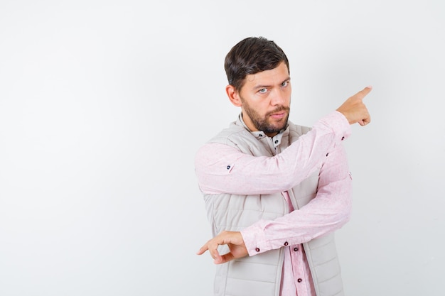 Portrait d'un bel homme pointant vers le coin supérieur droit en gilet, chemise et l'air confiant