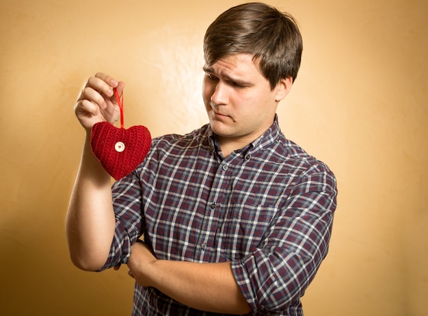 Portrait d'un bel homme regardant avec méfiance sur le coeur rouge décoratif