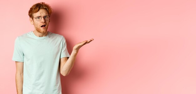 Portrait d'un bel homme rousse dans des verres à la bouche ouverte et confus regardant fixement l'appareil photo ne peut pas und