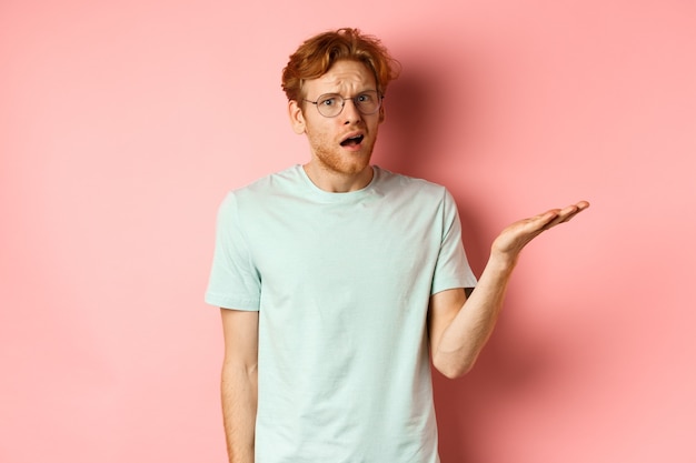 Portrait d'un bel homme rousse dans des verres à la bouche ouverte confuse et regarder la caméra ne peut pas und...