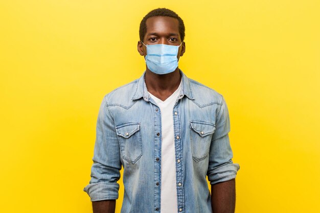 Portrait d'un bel homme sérieux et affirmé avec un masque médical à manches retroussées qui a l'air intelligent et professionnel, pigiste ou employé. studio d'intérieur tourné isolé sur fond jaune