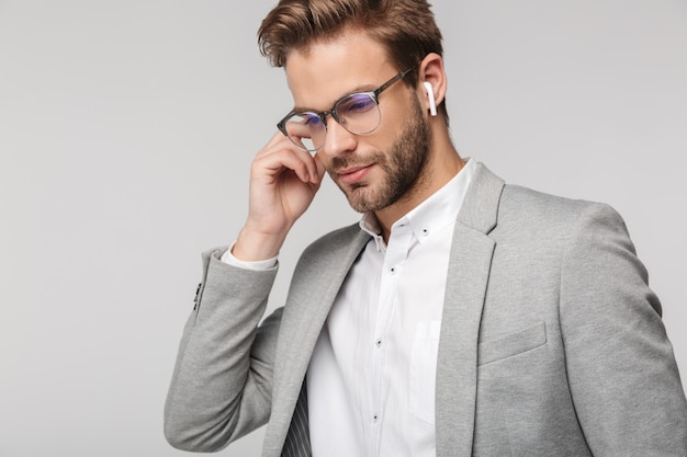 Portrait d'un bel homme sérieux à lunettes utilisant des écouteurs isolés sur un mur blanc