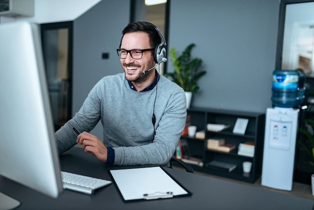 Photo portrait d'un bel homme souriant avec casque travaillant sur l'ordinateur.