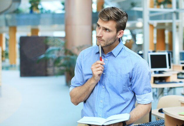 Portrait d'un bel homme souriant en chemise décontractée prenant des notes sur le lieu de travail