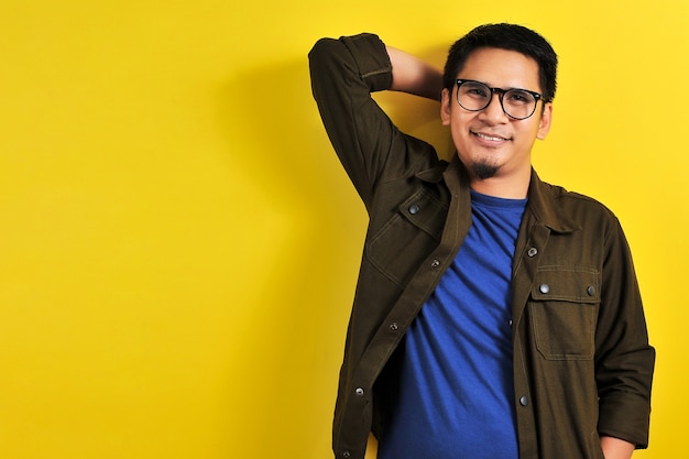 Portrait d'un bel homme souriant en t-shirt bleu, veste et lunettes, isolé sur fond jaune